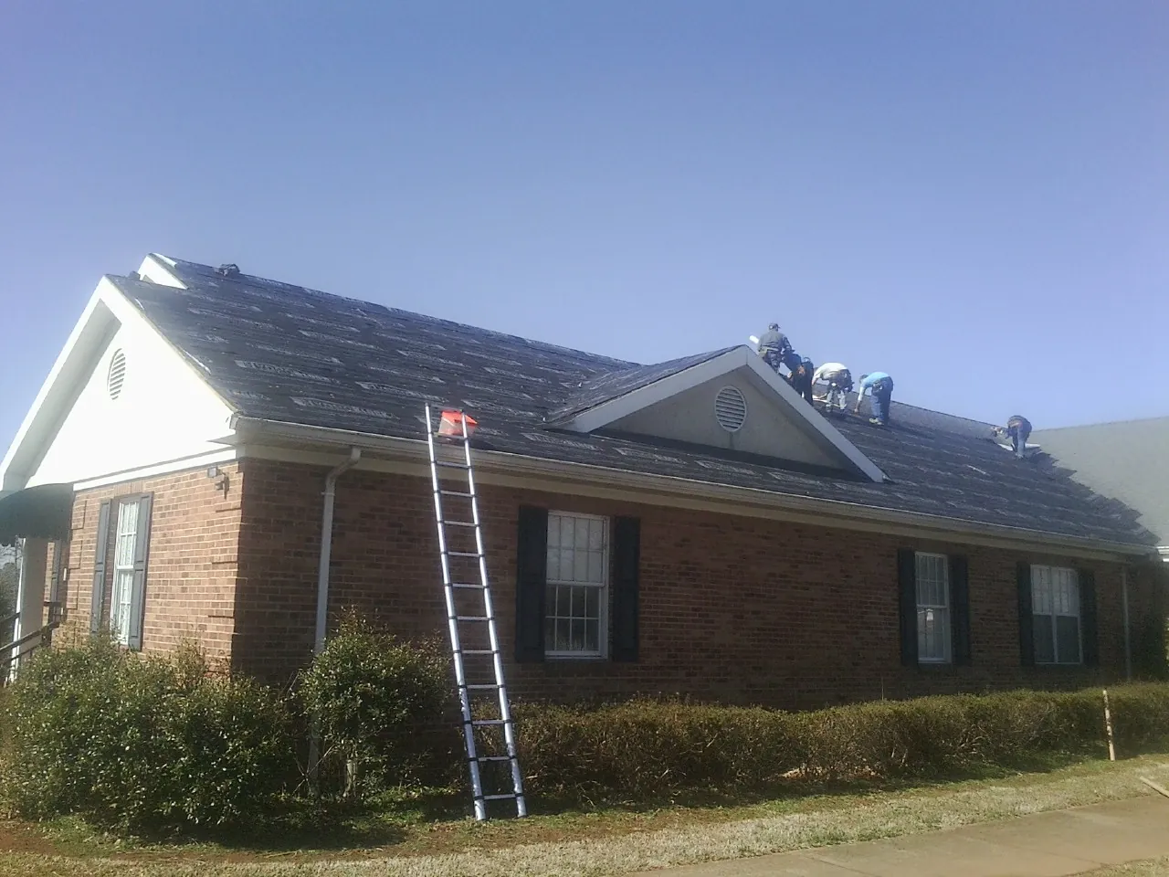 Crew tearing shingles off a brick ranch roof with a ladder set — Metal Roof Repair work by our crew in East Canton