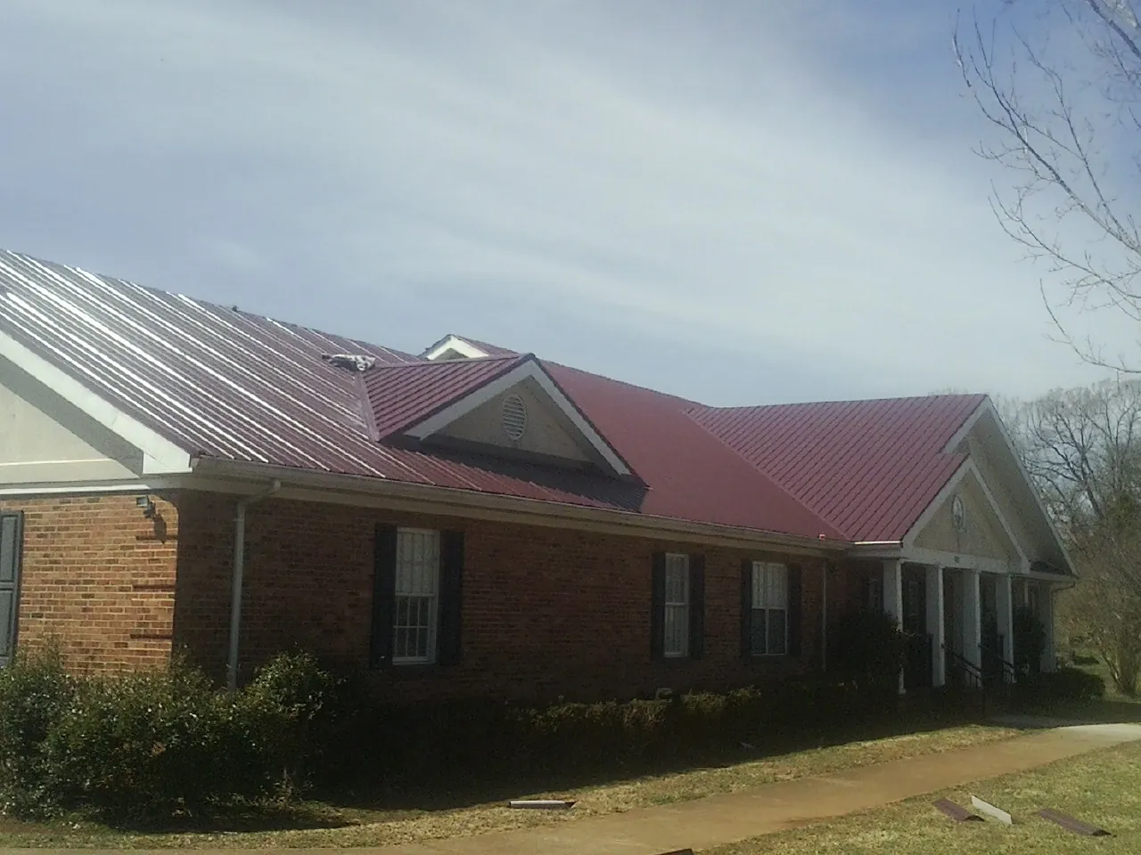 Red metal roof with gabled entries on a long brick building, from a Hail Damage Roof Repair job in East Canton