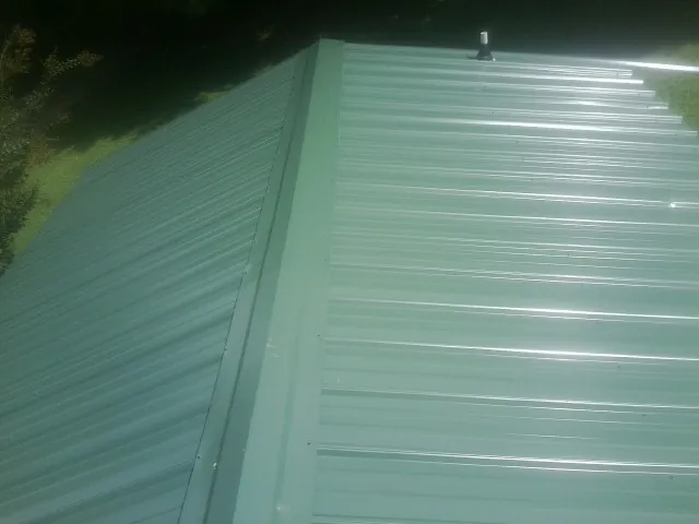 New green metal panels meeting at the ridge of a roof — Flat Roof Repair work by our crew in East Canton