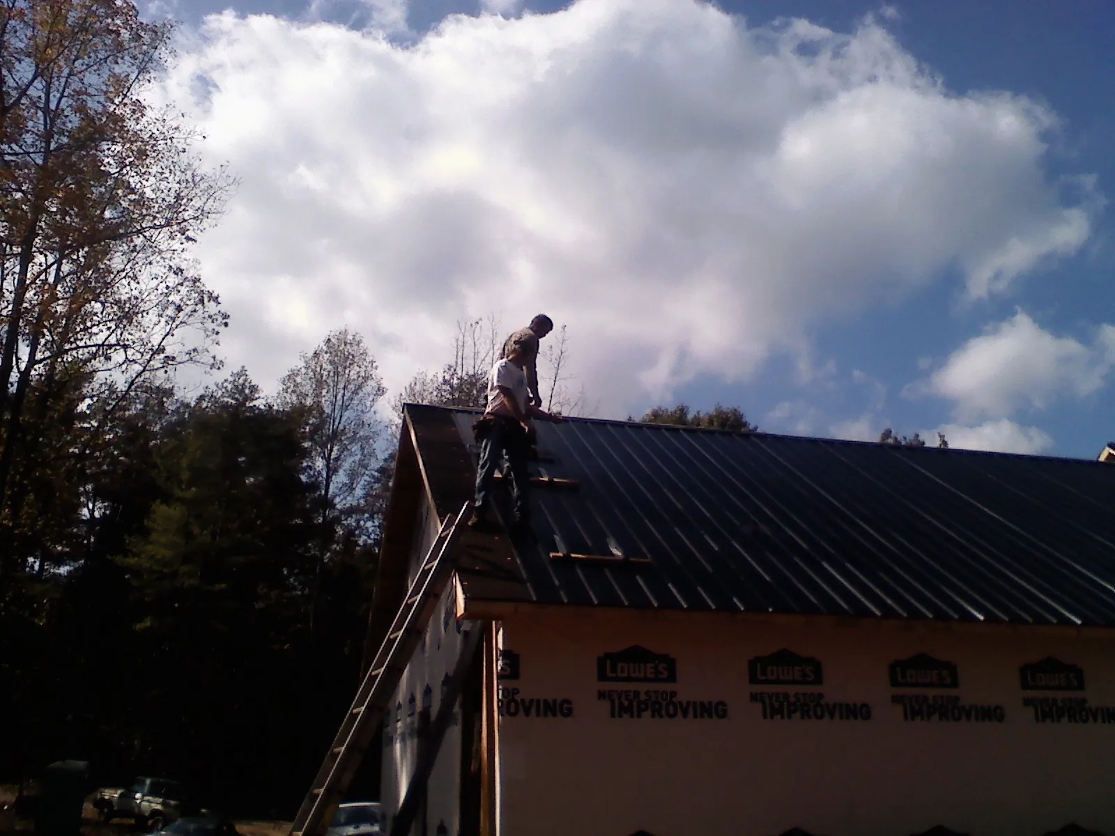 Roofer fastening dark metal panels high against a cloudy sky, from a Roof Inspection job in East Canton