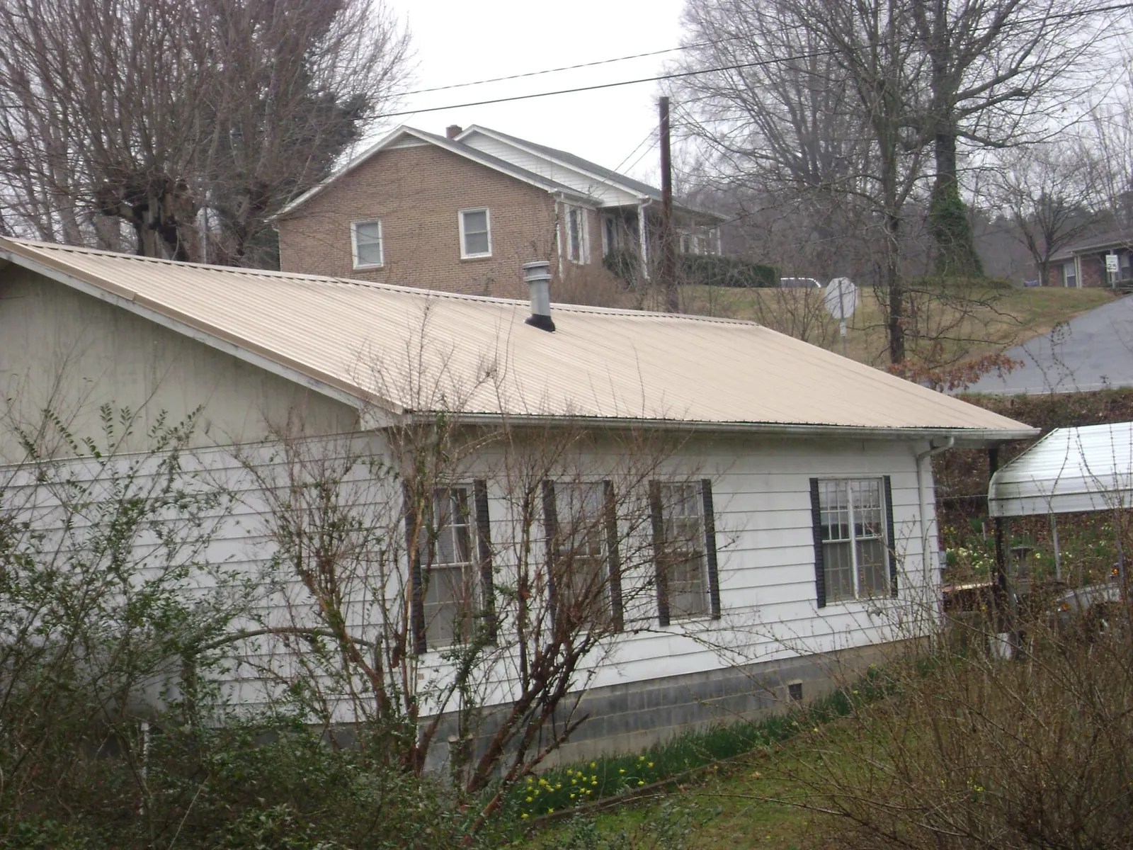 Tan metal roof on a white sided house set into a hillside — Commercial Roofing by Roofing Brothers in East Canton